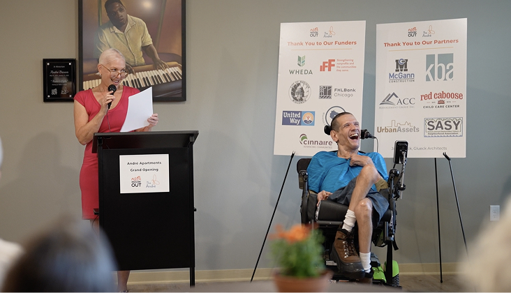 Woman reading from a podium with man in a wheelchair next to her