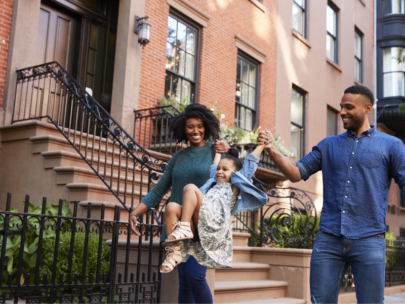 Mom and Dad swinging their daughter in front of apartment buildings